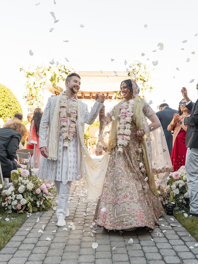 Anika and Caden walk through falling petals after the ceremony