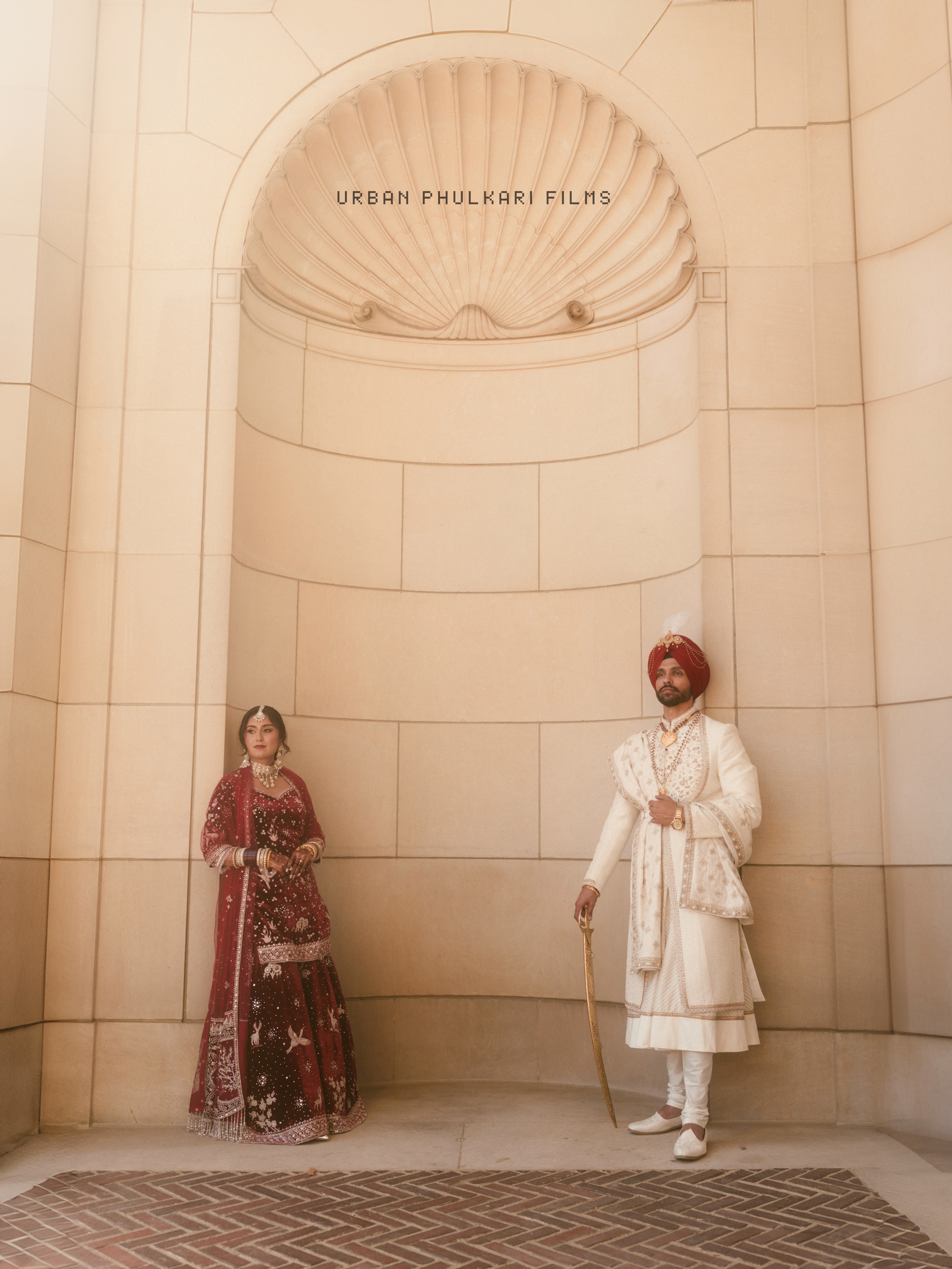 Banpreet and Yugraj beneath a pale stone arch at their wedding
