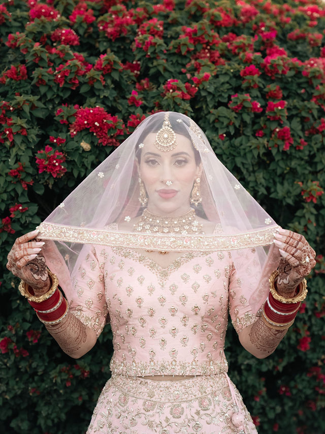 Aman lifts her veil beside red flowers