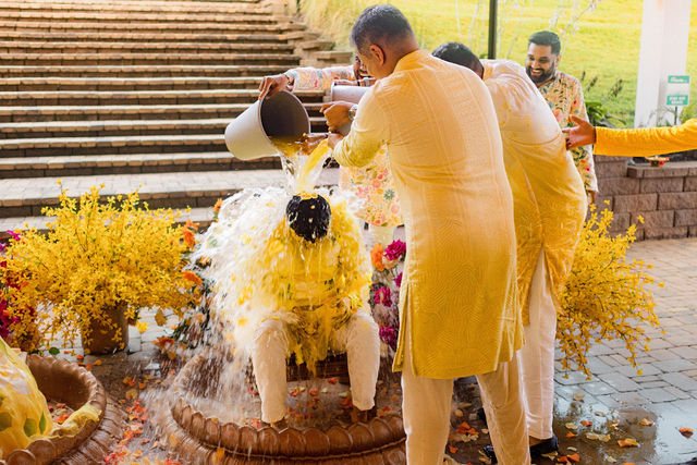 Loved ones playfully pouring water at Bishal’s Haldi