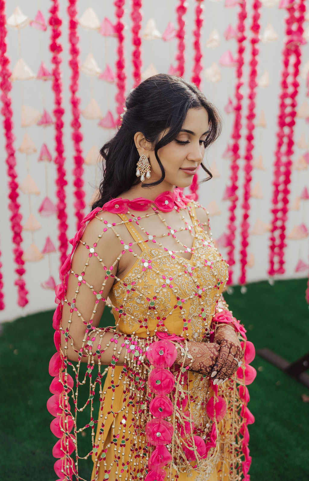The bride in a yellow outfit against a pink floral Haldi backdrop