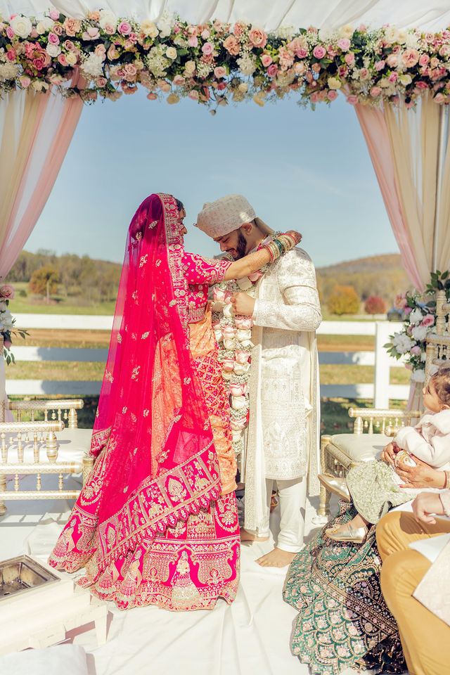 Monali and Sunny exchanging garlands beneath the floral mandap