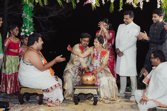 Rachana and Anoop smiling during a wedding ritual as family looks on