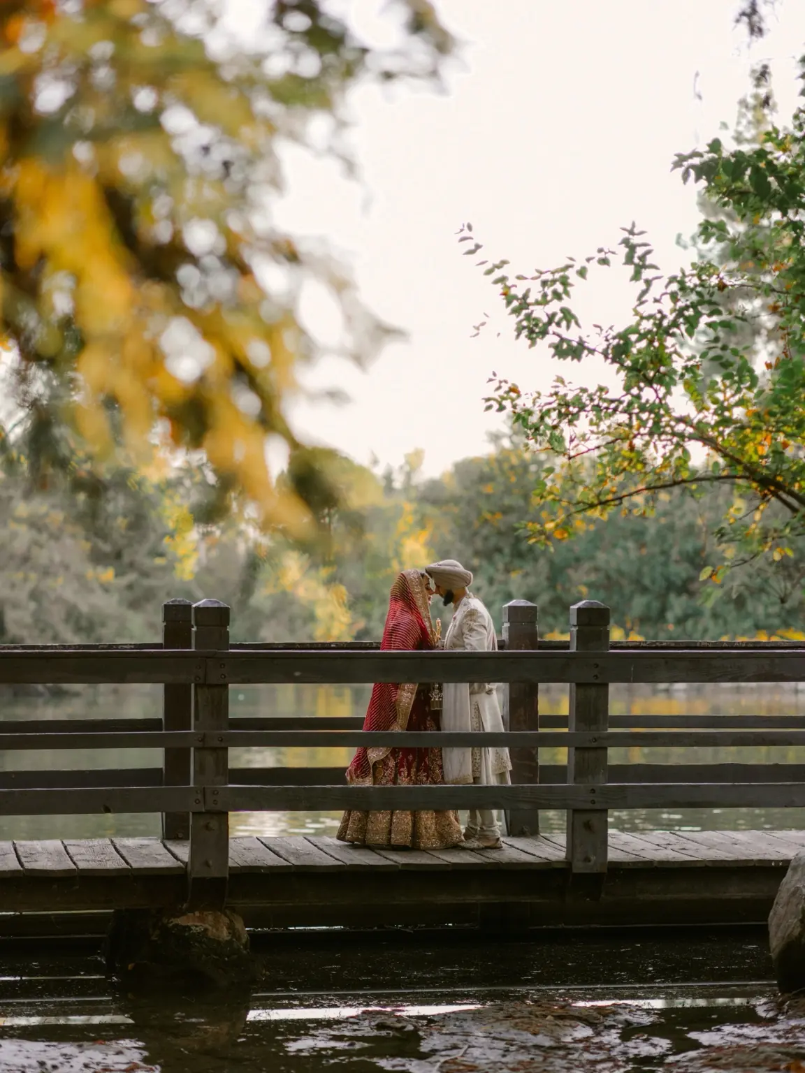 The couple share a kiss on a bridge beside the water at Woodward Park