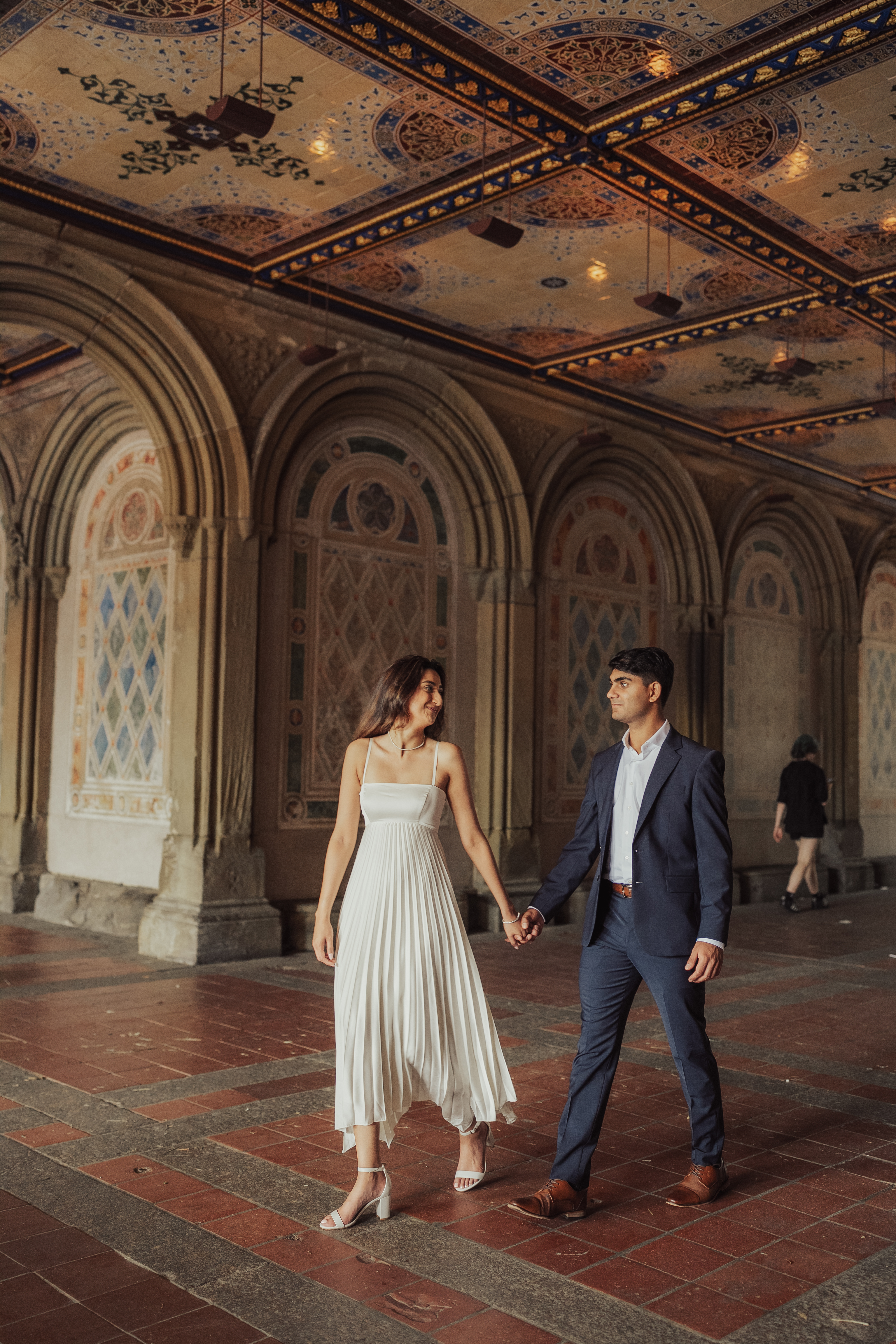 Richa and Shahil holding hands beneath an ornate painted ceiling