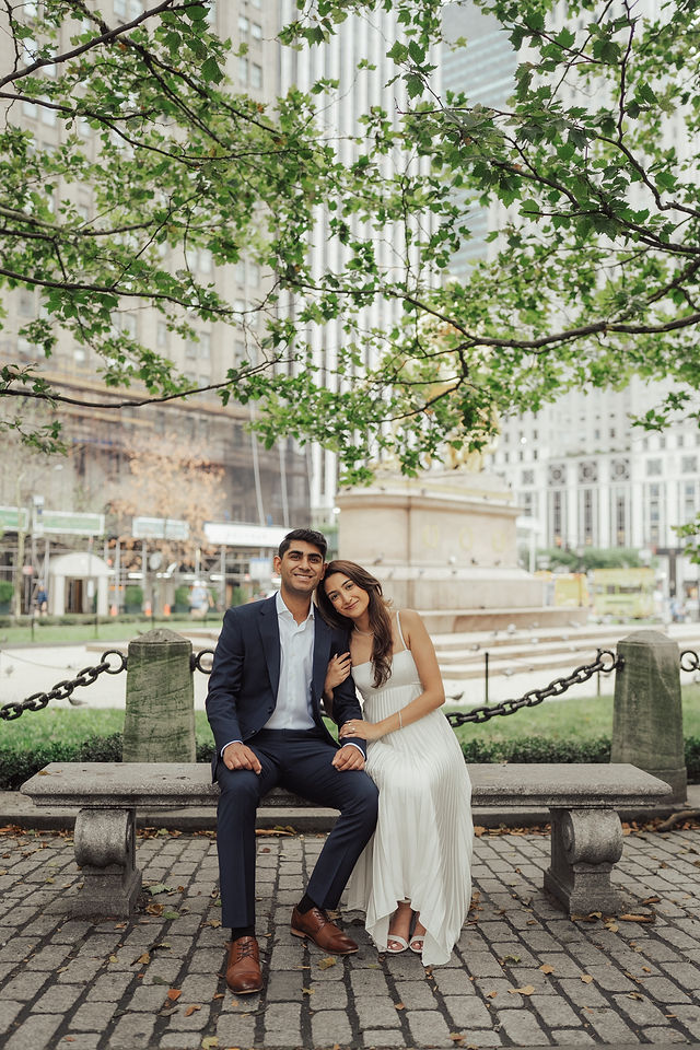 Richa and Shahil seated together beneath trees beside a New York square