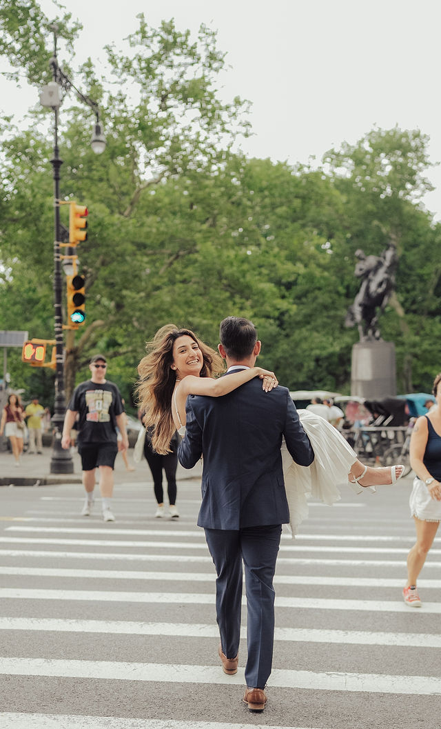 Shahil carrying a smiling Richa across a New York crosswalk