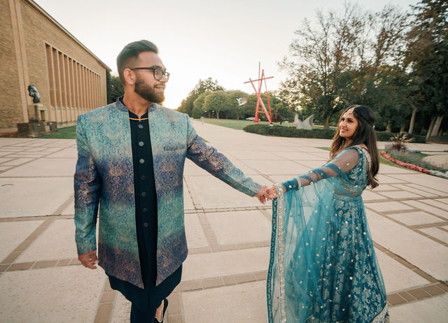 Mayank reaching toward Vidhi as they walk past a modern stone building