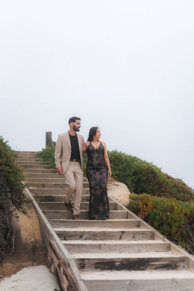 Varun and Nirali stand together on coastal steps beneath an open sky