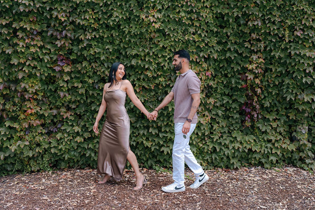 Varun and Nirali hold hands beside an ivy-covered wall